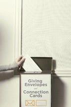 Hand placing an envelope in the donation box.