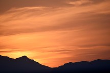 silhouettes of mountains at sunrise against an orange sky 
