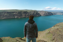 a man standing at the edge of a cliff and looking over into the water 