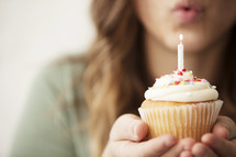 A woman blowing out a candle on a birthday cupcake 