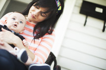 A young mother holds her infant son on the front porch.