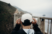 man, looking at a bridge connecting two mountains near the ocean 