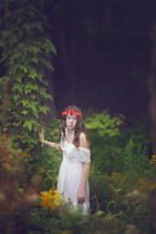 a girl standing in a garden with a crown of flowers in her hair 