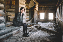A girl sits in an abandoned log house.