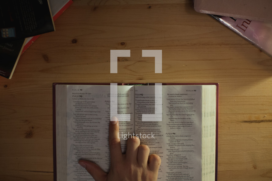 Hand pointing to scripture in a Bible on a wooden table.