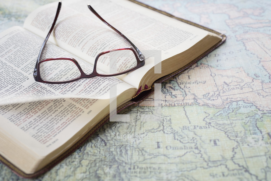 reading glasses on an open Bible on a map 
