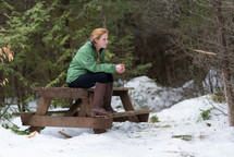 a teen girl sitting on a picnic table outdoors in snow 
