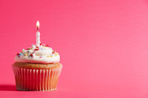 cupcake and candle against a pink background 