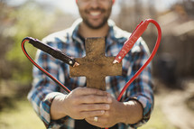 Smiling man holding cross with jumper cables attached.