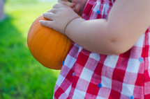 a toddler carrying a small pumpkin