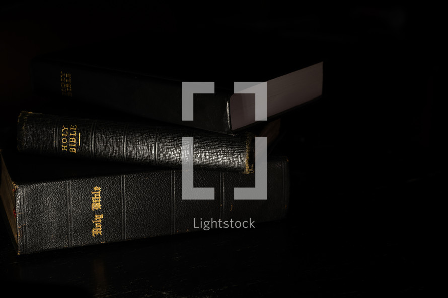 stack of three Bibles on a black background 