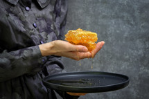 Female Hand Holdong Fresh Honey In Honeycomb over a Plate