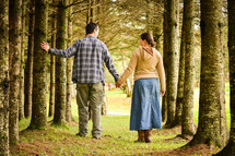 a couple walking holding hands through a forest 