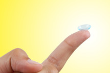 Contact lens on finger isolated on yellow background