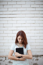 Woman clutching a Bible to her chest, praying outside in front of a brick wall.