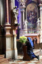 Nun at prayer before a statue of the Mother Mary and baby Jesus in a Catholic Cathedral.