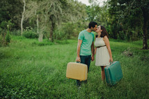 newly weds holding suitcases kissing 