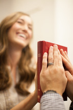 Husband and wife with their hands on either side of a Bible.