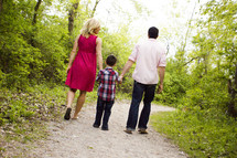 Back view of mother, father and son walking dow a wooded path