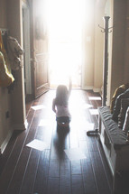 Silhouette of a girl waving goodbye in a sunlit doorway surrounded by papers on the wood floor.