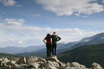 Embraced couple standing on rocks near a mountain range.