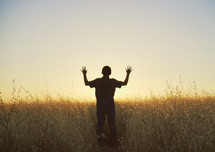 silhouette of a young man with raised hands standing in a field 