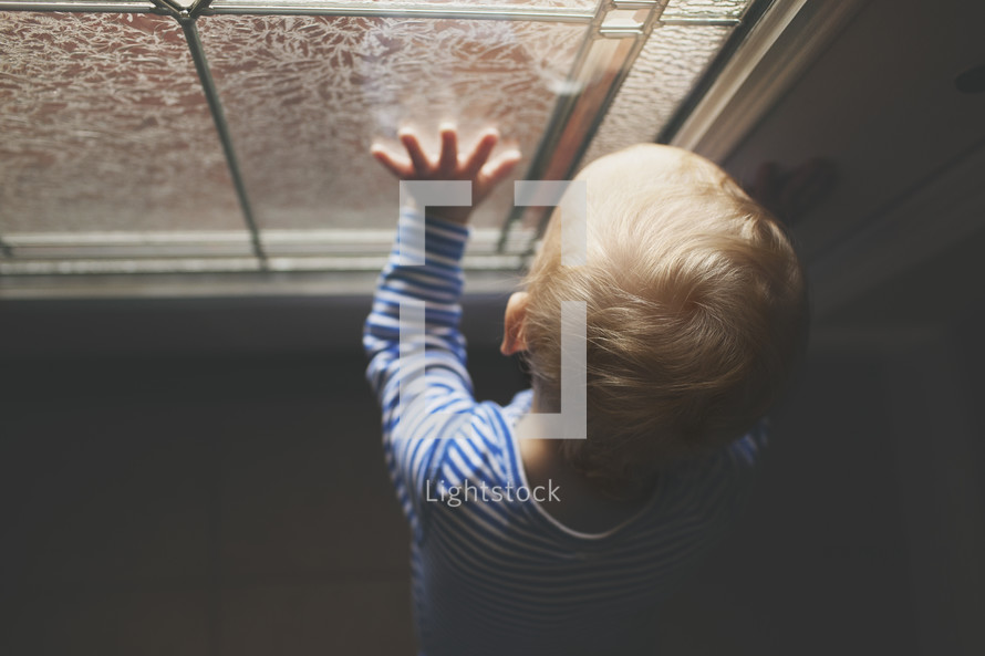 a toddler boy with his hand on a window 