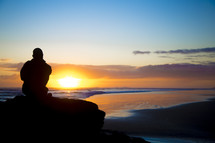 man sitting on a rock on a beach at sunset 