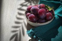 Bowl of plums with leaf shadow