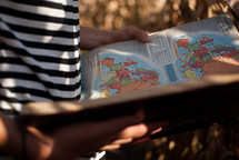 Hands holding an open book of maps.