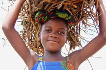A little African girl carrying a bundle of sticks over her head 