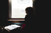 a child looking out a window and an open Bible 