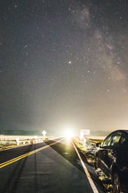 stars in a night sky and lights from a highway 