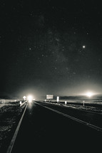 stars in a night sky and lights on a highway 