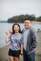 a couple standing on a river shore giving peace signs 