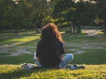 a person sitting on a blanket reading in a park 