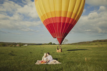 A couple kissing on a blanket with a hot air balloon in the background