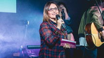 a woman holding a Bible and microphone on stage 