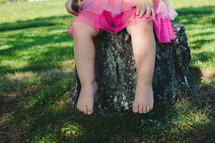 legs of a toddler girl sitting on a stump 