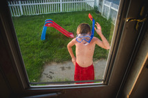 a little boy at the back door wearing a snorkel and googles 