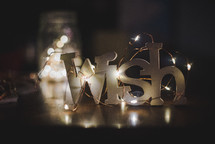 Fairy lights surrounding the word Wish that is sitting on a table.