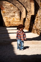 toddler in a cowboy hat walking on an arched covered walkway