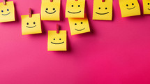 Happy faces drawn on yellow sticky notes on a pink magenta background. 