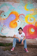 boy sitting in front of a street art painted wall 