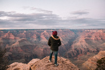 a man standing at the edge of a cliff looking out at canyons 