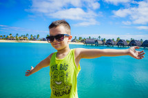 a boy in sunglasses standing in front of cabins on stilts 