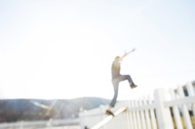 A boy jumping over a fence into the sunlight. 