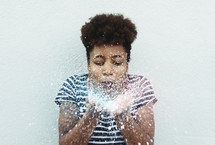 a woman blowing on and spraying water in her cupped hands 