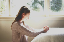 a teen kneeling in prayer by her bedside 