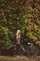 blonde woman standing outdoors next to a bicycle 